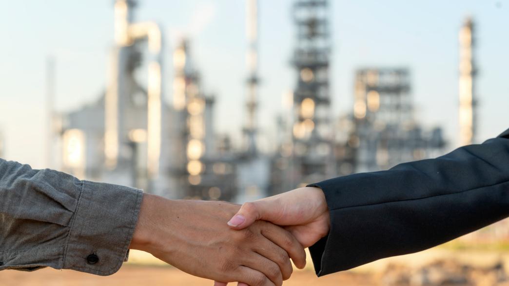 Two business persons shaking hands over oil refinery plant of petroleum