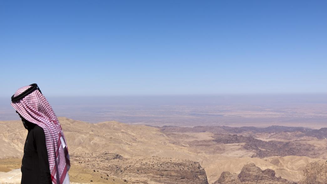 A young sheikh (with his traditional red/white Keffiyeh) in front of a desert landscape