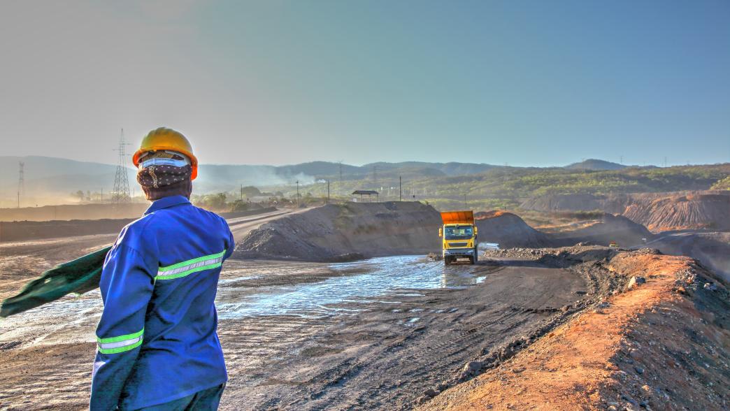 A worker directs heavy trucks and machinery in an open mine in Zambia.