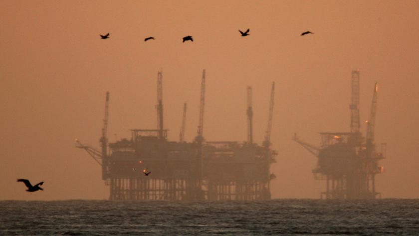 Offshore oil rigs seen in the dust at sunset with birds flying in the background