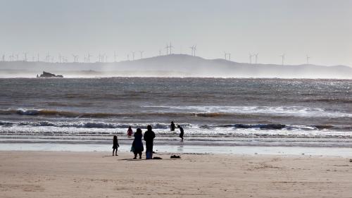 People beach in Morocco with wind turbines in the background