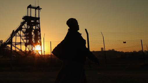 A woman walks past a derelict gold mine shaft's winding gear in front of the setting sun in Johannesburg, South Africa