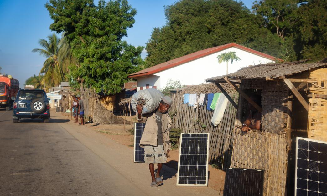 Local residents of Morondava engage in daily activities with solar panels lining the roadside in Madagascar's vibrant village life. Image includes solar panels